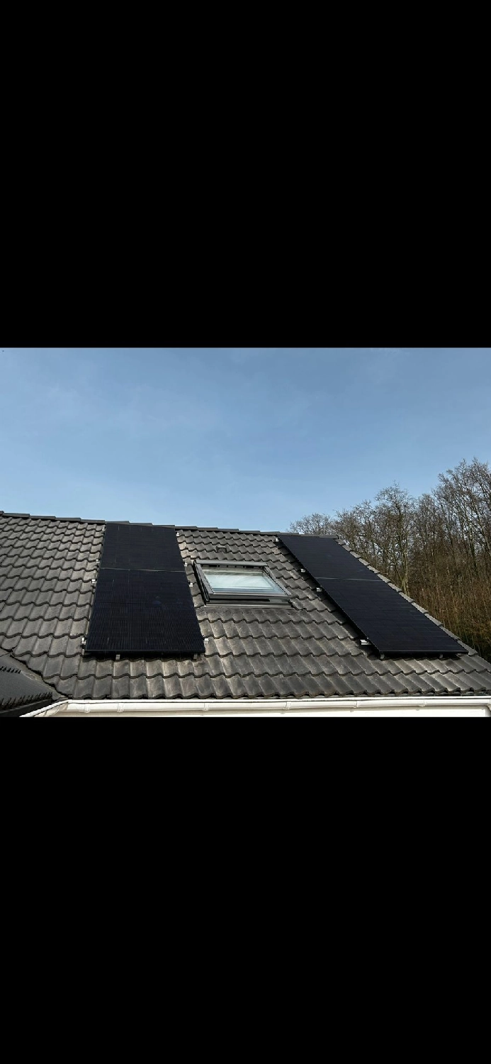 Spanndecken Grunau - Sanierung, Renovierung & Innenausbau - Schwarze Solarpaneele, die auf einem Ziegeldach neben einem Dachfenster installiert sind.
