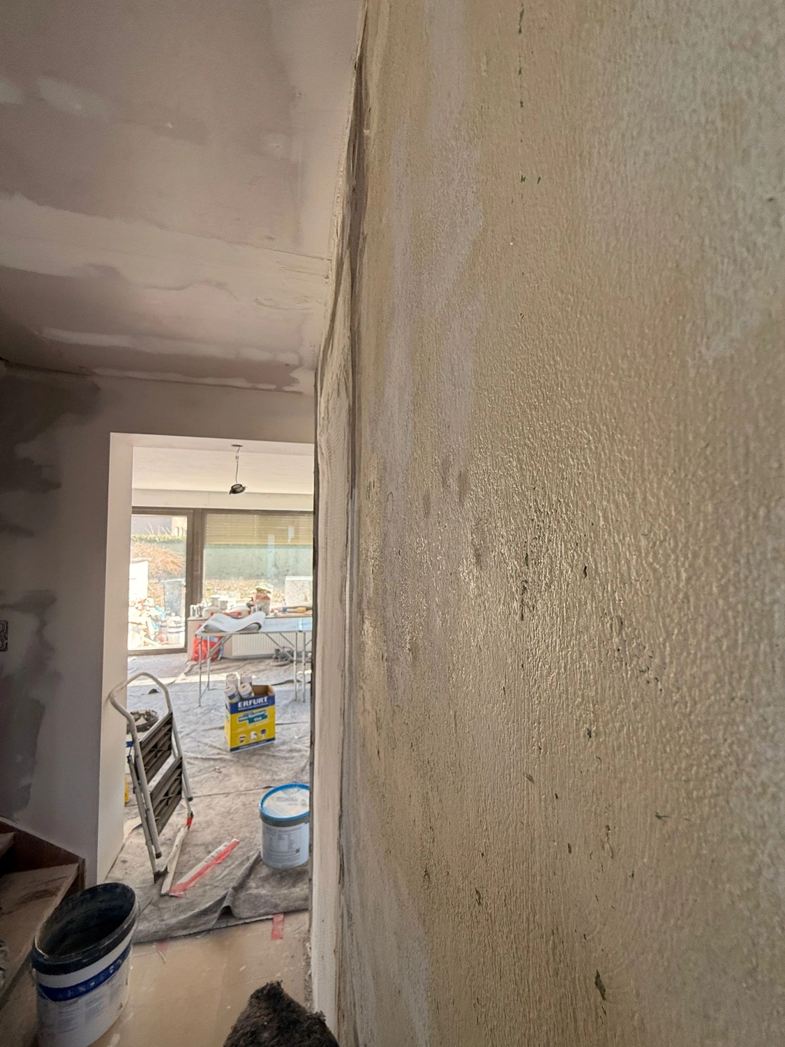 Spanndecken Grunau - Sanierung, Renovierung & Innenausbau - Eckansicht von strukturierten Putzwänden mit Blick in einen angrenzenden Raum mit Baumaterialien.