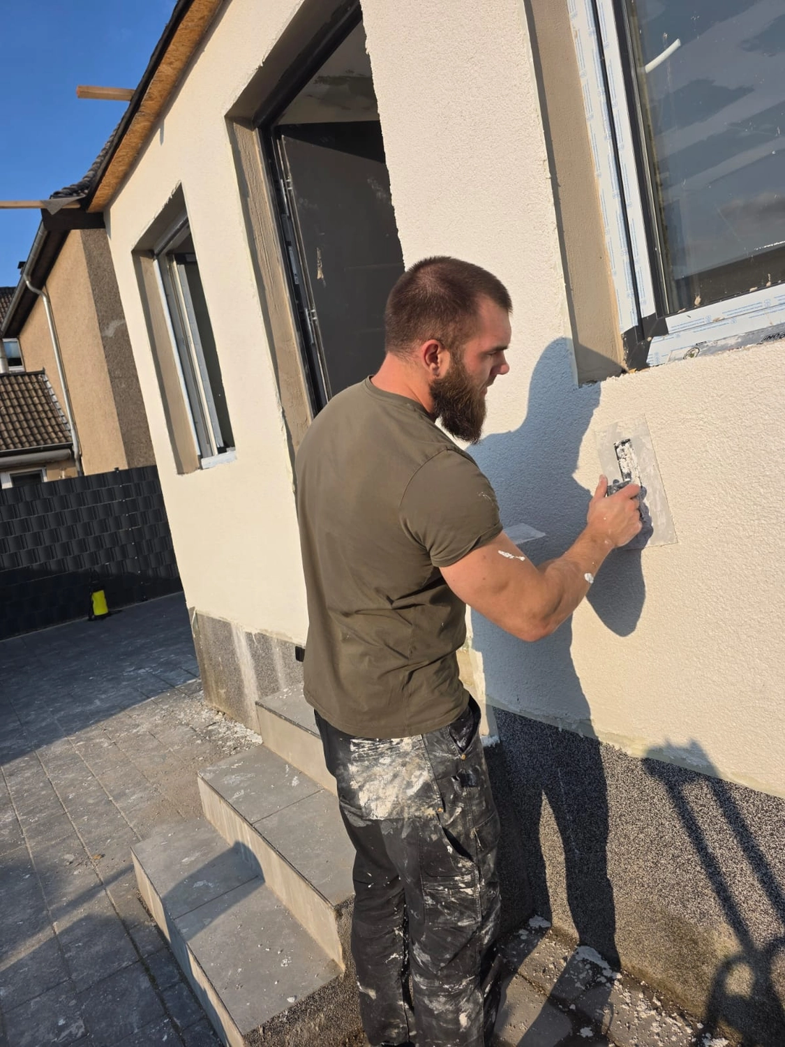 Spanndecken Grunau - Sanierung, Renovierung & Innenausbau - Ein Mann mit Bart verputzt eine Außenwand mit einer Kelle.