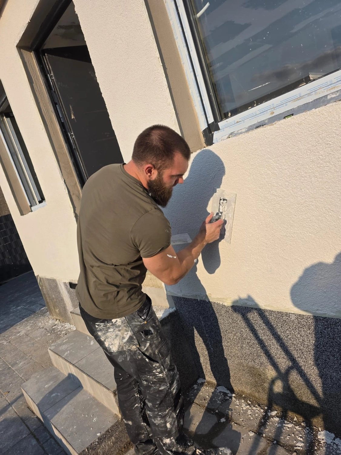 Spanndecken Grunau - Sanierung, Renovierung & Innenausbau - Ein Mann hockt sich hin, um den unteren Teil einer Außenwand auszubessern und zu glätten.