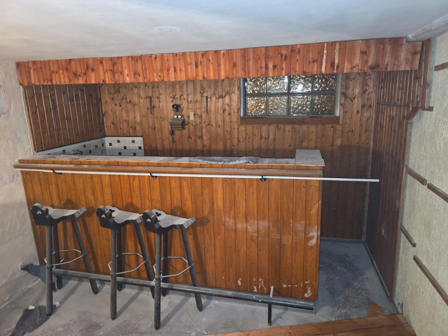 Spanndecken Grunau - Sanierung, Renovierung & Innenausbau - Eine altmodische Kellerbar mit dunkler Holzvertäfelung, Barhockern und einem kleinen Glasbausteinfenster.