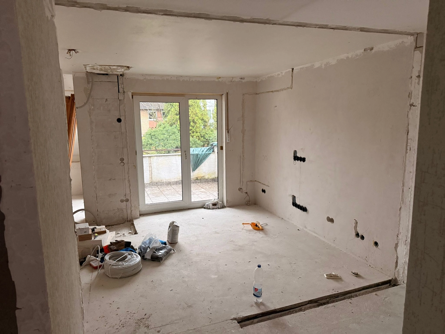 Spanndecken Grunau - Sanierung, Renovierung & Innenausbau - Unfertige Wohnzimmerrenovierung mit freiliegendem Betonboden, verputzten weißen Wänden und einer Glasschiebetür zur Terrasse.