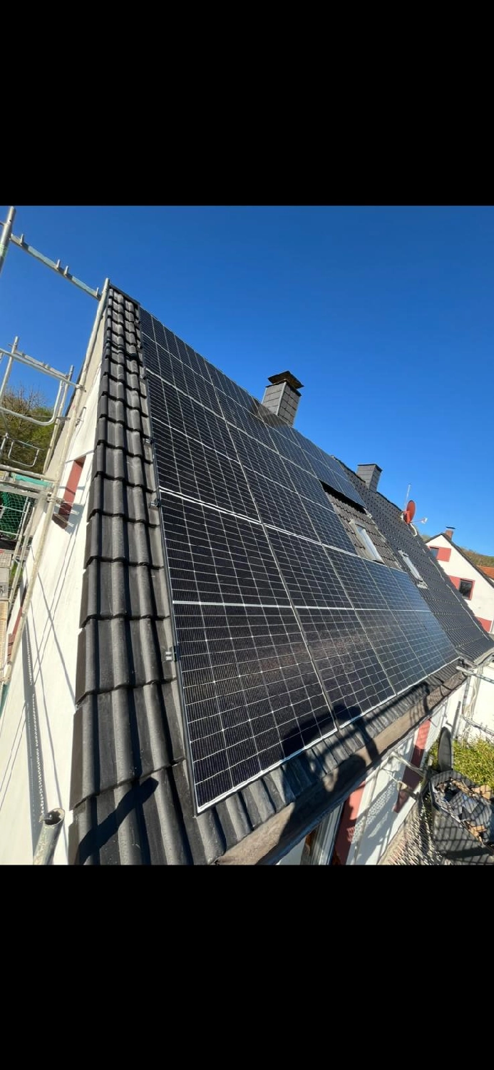 Spanndecken Grunau - Sanierung, Renovierung & Innenausbau - Eine große Anlage aus modernen schwarzen Solarmodulen, installiert auf einem steilen, dunkel gedeckten Ziegeldach unter strahlend blauem Himmel.