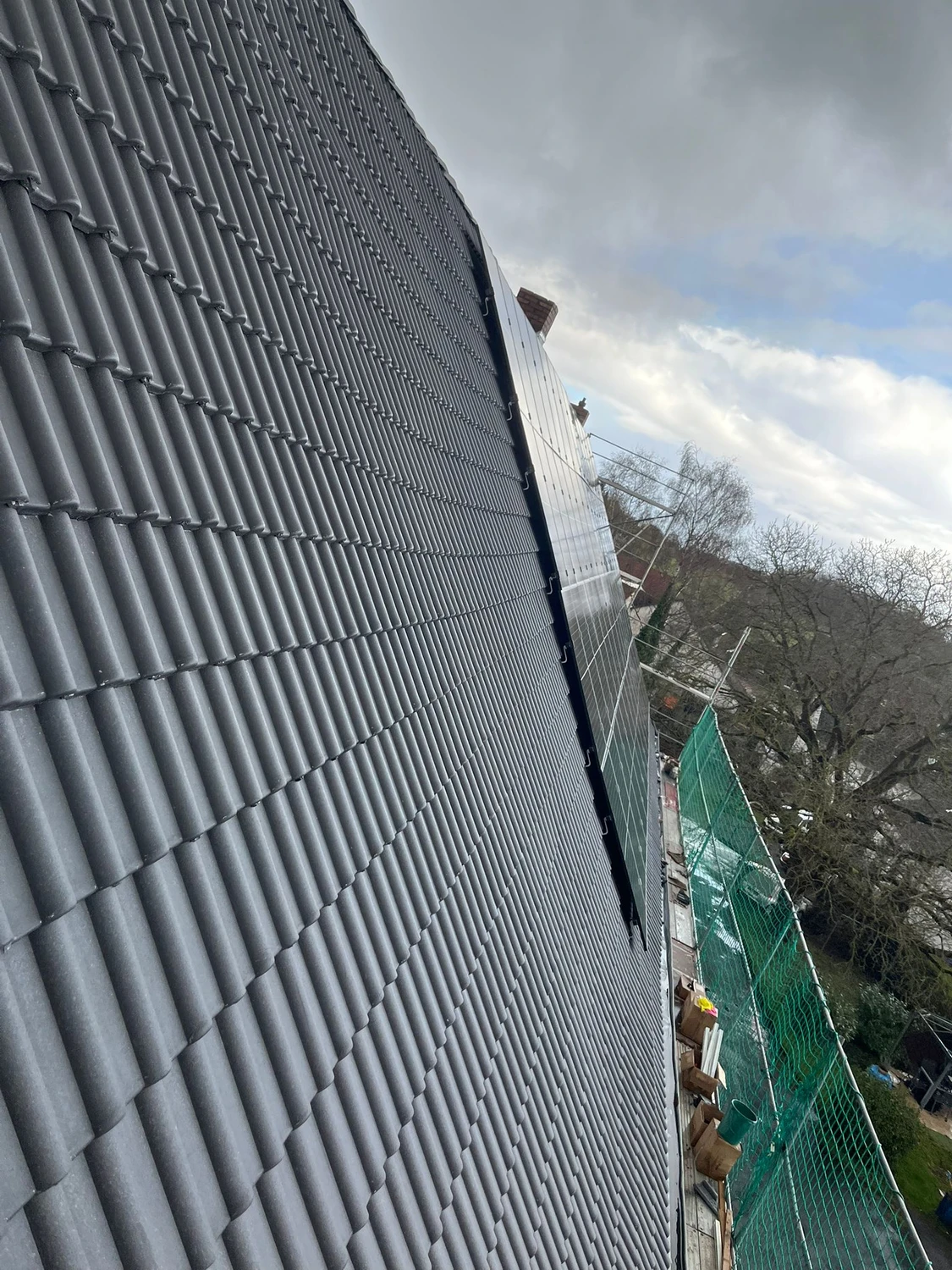 Spanndecken Grunau - Sanierung, Renovierung & Innenausbau - Eine große Anlage aus modernen schwarzen Solarmodulen, installiert auf einem steilen, dunkel gedeckten Ziegeldach unter strahlend blauem Himmel.