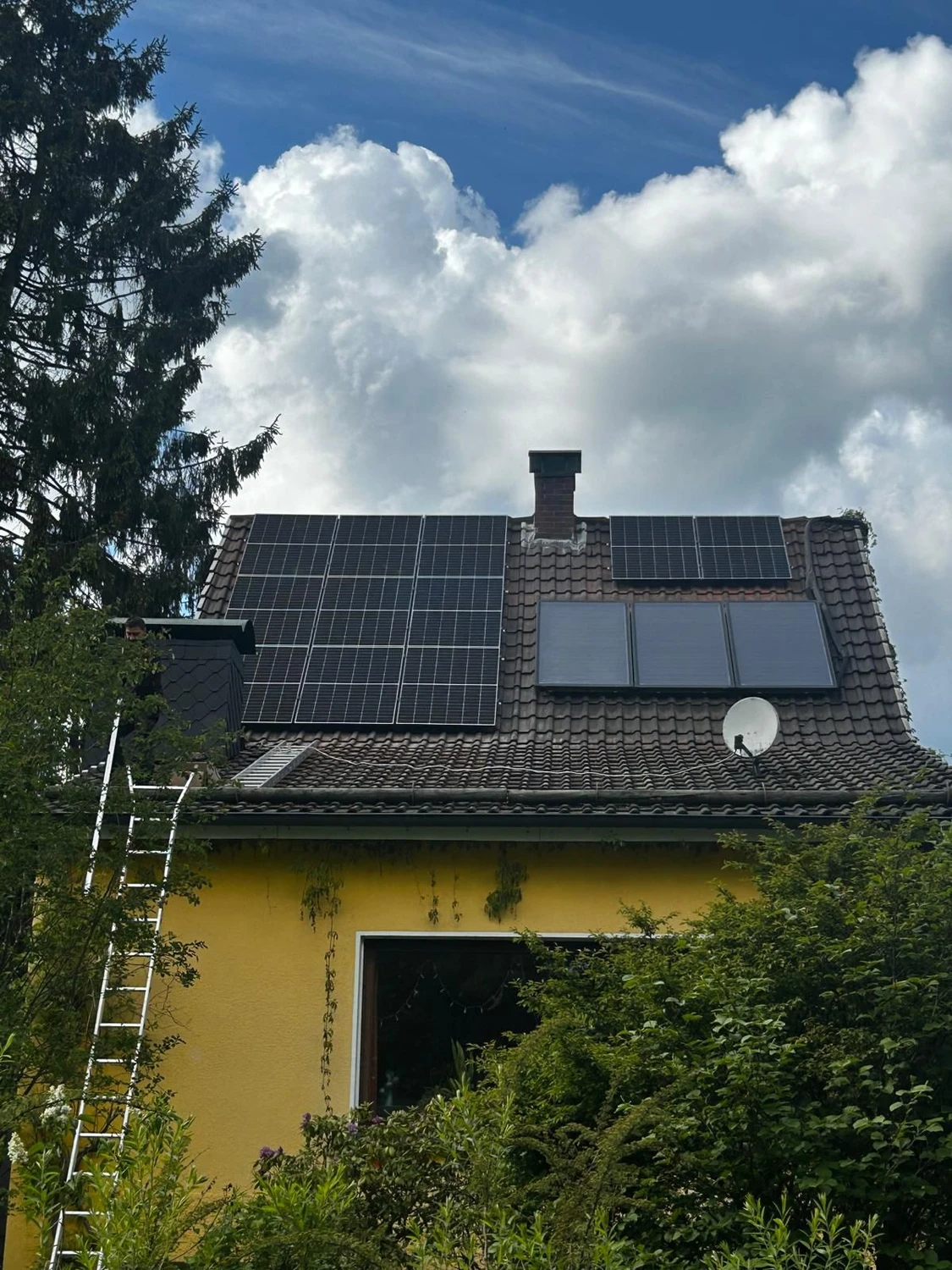 Spanndecken Grunau - Sanierung, Renovierung & Innenausbau - Eine große Anlage aus modernen schwarzen Solarmodulen, installiert auf einem steilen, dunkel gedeckten Ziegeldach unter strahlend blauem Himmel.