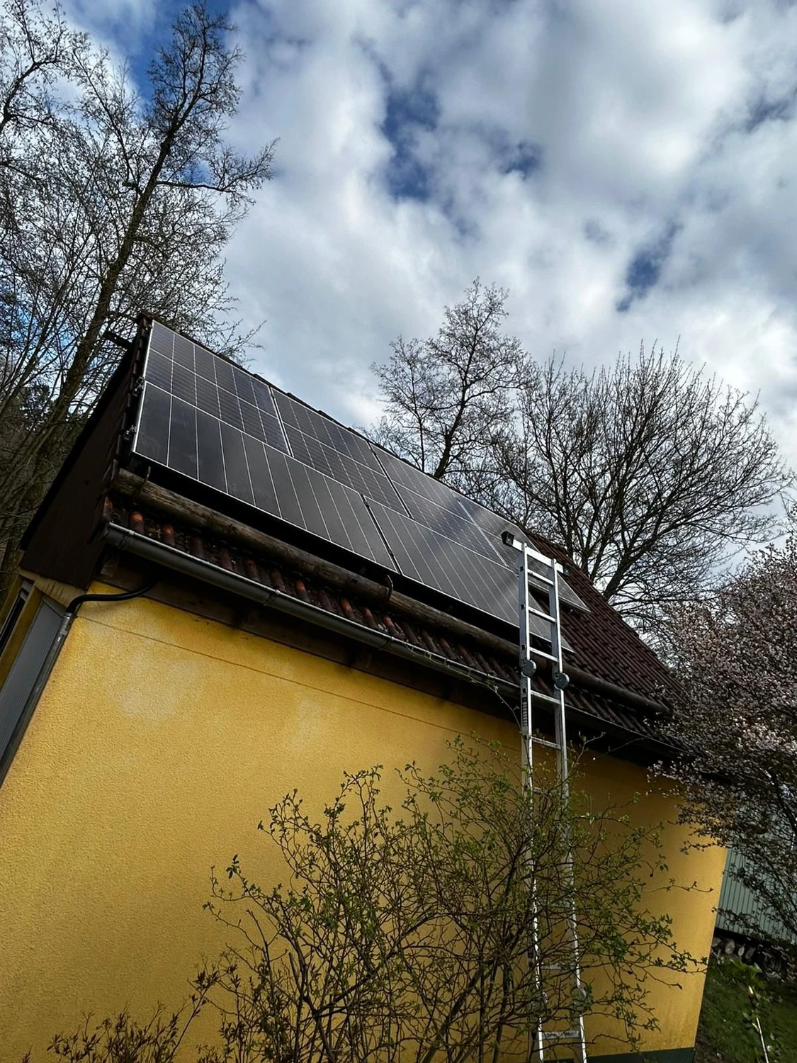 Spanndecken Grunau - Sanierung, Renovierung & Innenausbau - Eine große Anlage aus modernen schwarzen Solarmodulen, installiert auf einem steilen, dunkel gedeckten Ziegeldach unter strahlend blauem Himmel.