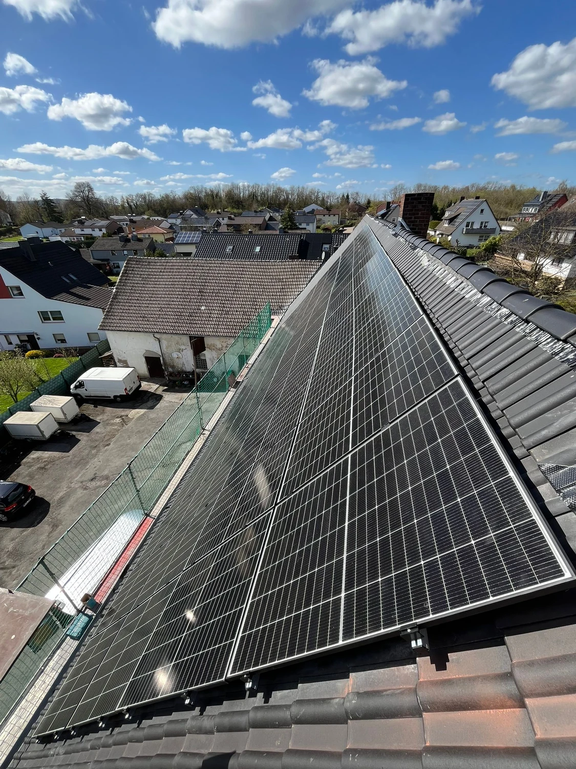 Spanndecken Grunau - Sanierung, Renovierung & Innenausbau - Eine große Anlage aus modernen schwarzen Solarmodulen, installiert auf einem steilen, dunkel gedeckten Ziegeldach unter strahlend blauem Himmel.