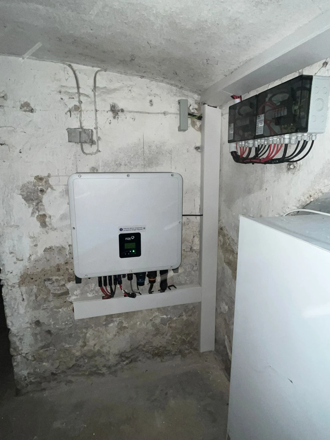 Spanndecken Grunau - Sanierung, Renovierung & Innenausbau - Ein wandmontierter Fox ESS Solarwechselrichter an einer Betonwand neben Stromverteilerkästen.
